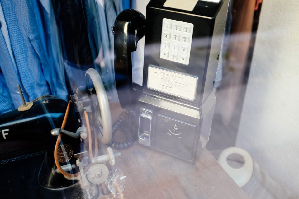 Old payphone and sewing machine behind a shop window glass