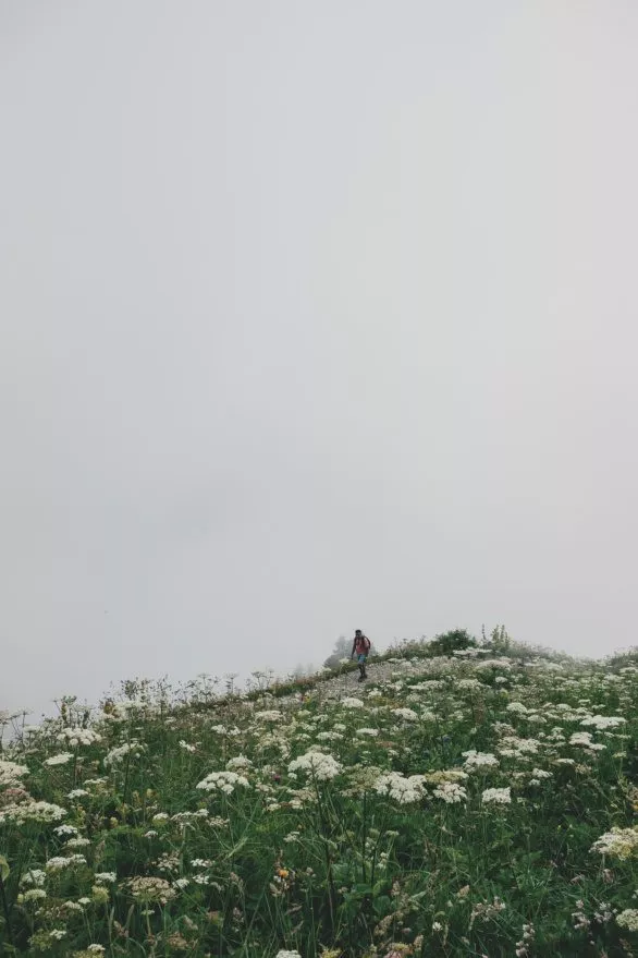 Hiker goes up a mountain slope in thick clouds