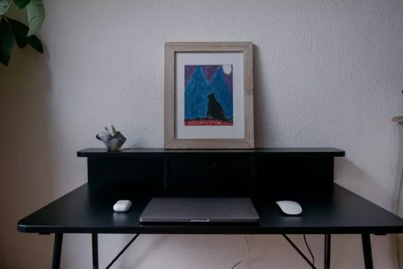 Closed laptop computer on a black table with framed painting, mo
