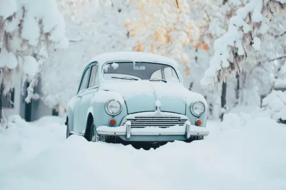 An old blue car is parked in the snow
