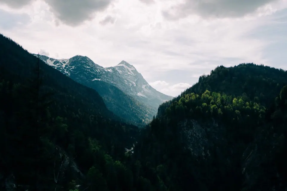 Snow-Capped Alps With Forested Valley Under Cloudy Sky