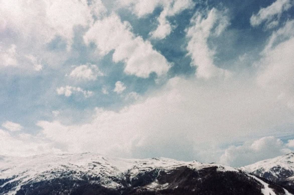 White puffy clouds float over a snow-capped mountain range